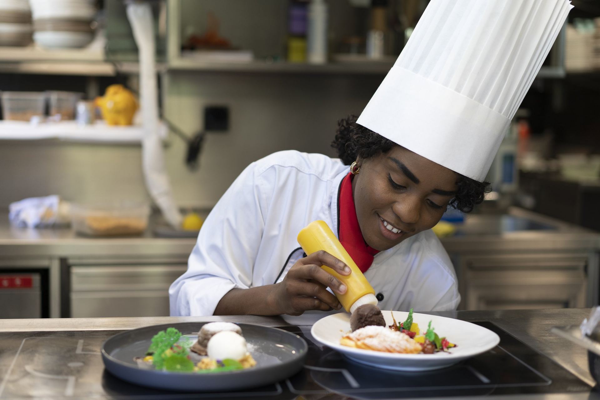 BHMS student in tall chef hat saucing plated desserts