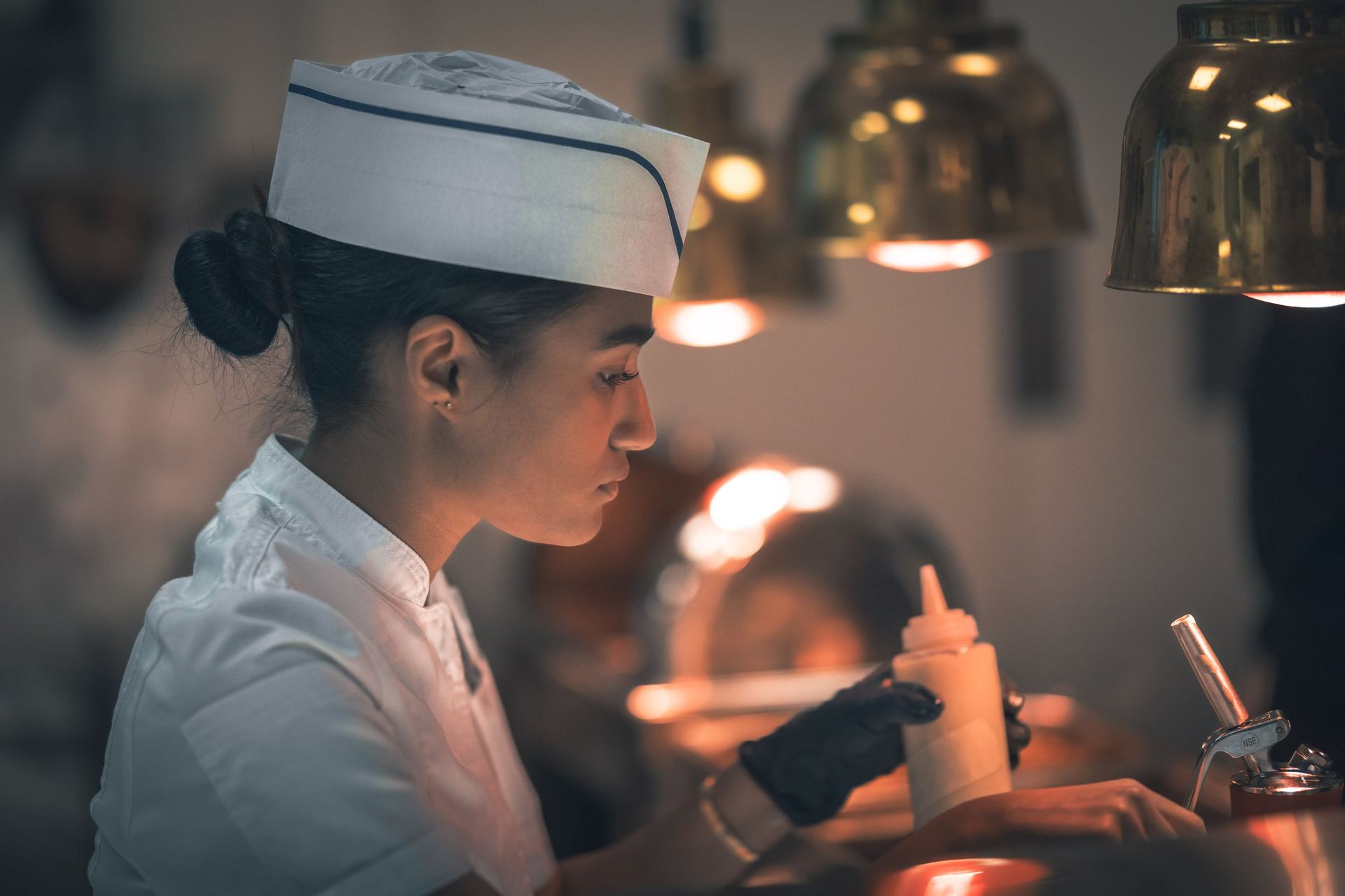 BHMS culinary student plating a dish under brass heat lamps