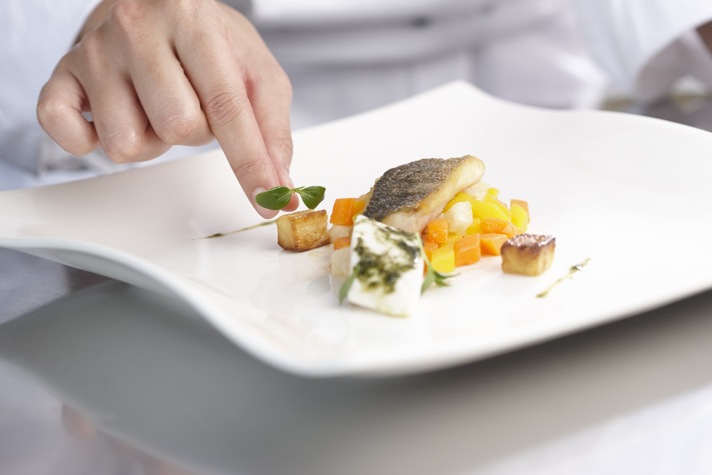 Close-up of a student placing microgreens on a plated dish