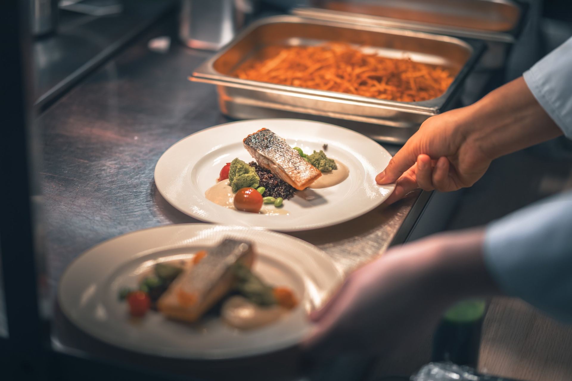 Plated dishes crossing the service pass in a BHMS kitchen